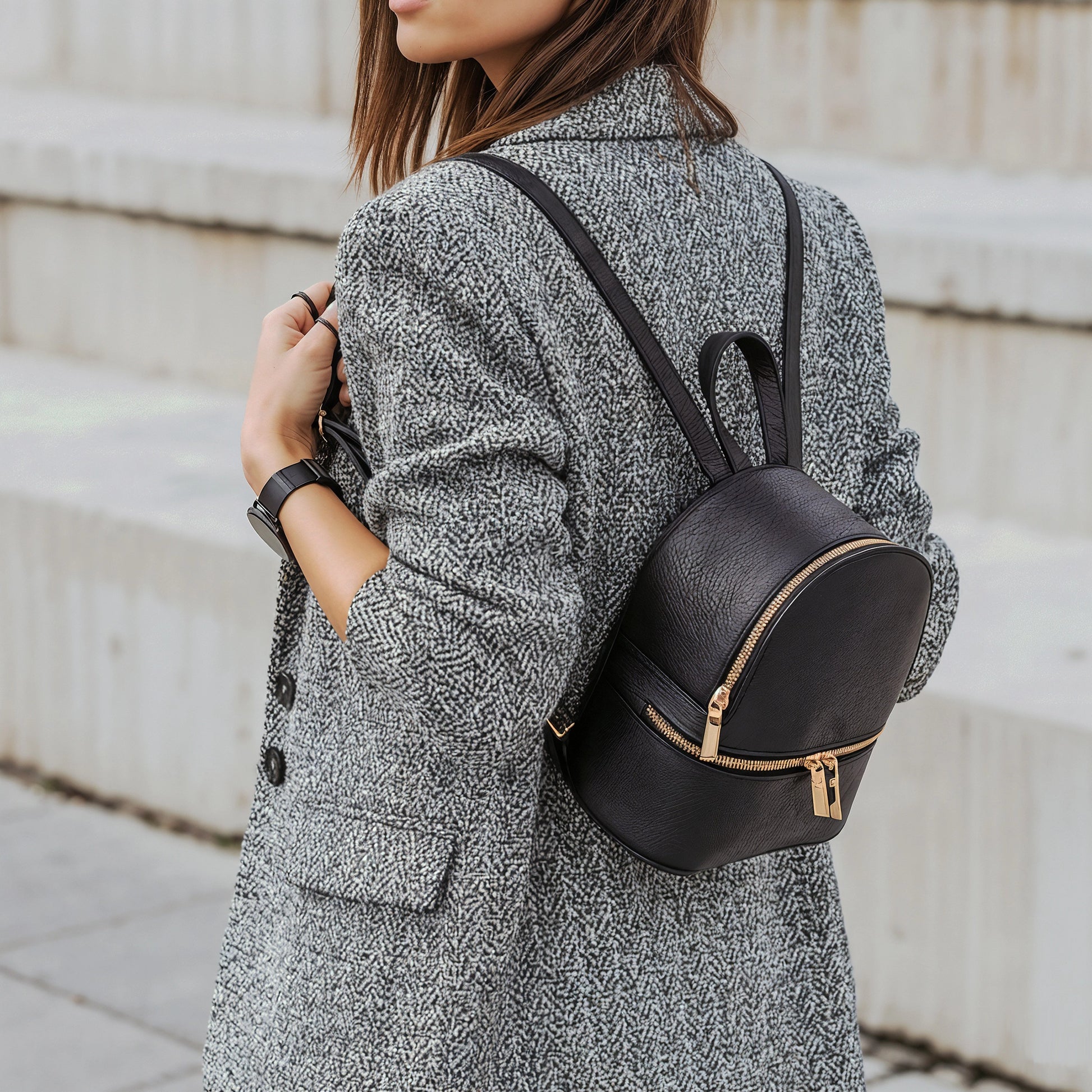 Woman wearing a grey textured coat carrying a black David Halfon leather backpack with gold zippers